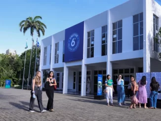 Instituições privadas de ensino com até 4 de dezembro para aderir ao Fies, prédio da faculdade UNIFOR com estudantes na frente, clima ensolarado, árvores e palmeiras ao fundo.