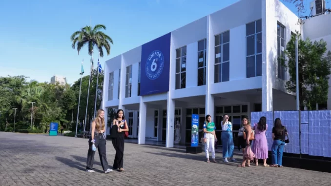 Instituições privadas de ensino com até 4 de dezembro para aderir ao Fies, prédio da faculdade UNIFOR com estudantes na frente, clima ensolarado, árvores e palmeiras ao fundo.