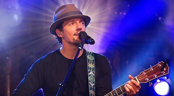 jason-mraz-turne-sul-americana-brasil-jpg Jason Mraz em performance ao vivo confirmando turnê sul-americana e cinco shows no Brasil, tocando guitarra e cantando em palco iluminado.
