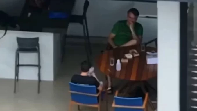 moraes-cobra-bolsonaro-por-celular-nikolas-visita Moraes cobra Bolsonaro por celular usado por Nikolas em visita, cena mostra duas pessoas discutindo na mesa com objetos ao redor, incluindo garrafas e documentos.