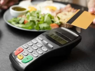Pessoa usando cartão de débito para pagar um almoço em um restaurante, com uma maquininha de pagamento e alimentos à sua frente, simbolizando benefícios do novo decreto