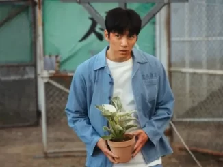 Cena do personagem principal de 'O Manipulado', destaque do suspense que domina Disney+ e conquista público em massa, com expressão séria segurando uma planta em cenário urbano.