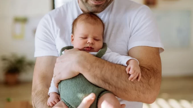 Pai segurando um bebê recém-nascido com expressão de carinho e proteção, simbolizando licença paternidade de até 20 dias após aprovação na Câmara.