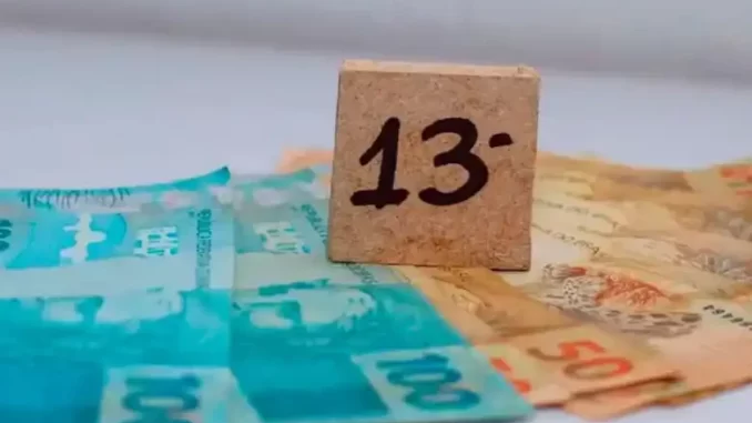 Dinheiro de cédulas brasileiras com bloco de madeira apontando o número 13, relacionado ao pagamento do 13º salário para trabalhadores.