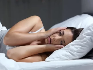 Mulher com insônia, deitada na cama e segurando a cabeça, ilustrando os impactos da privação de sono e estratégias clínicas para interromper o ciclo de exaustão.