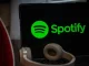 Imagem mostra logo do Spotify na tela de um laptop, com fone de ouvido na frente, indicando a polêmica sobre o processamento de streams falsos de Drake.