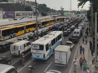 Tiroteio na Avenida Brasil no Rio de Janeiro causa bloqueio temporário, com trânsito congestionado, ônibus parados e pessoas caminhando na calçada, após troca de tiros.