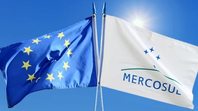 alianca-italia-franca-mercusul-ue-jpg Bandeira da União Europeia ao lado da bandeira do Mercosul balançando ao vento sob o sol, simbolizando possível aliança da Itália com a França e adiamento do acordo Mercosul-UE.