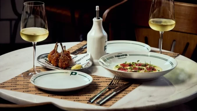 Mesa com pratos e taças de vinho em uma bodega e boteco do bairro Pinheiros, com pratos de comida e ambiente aconchegante.