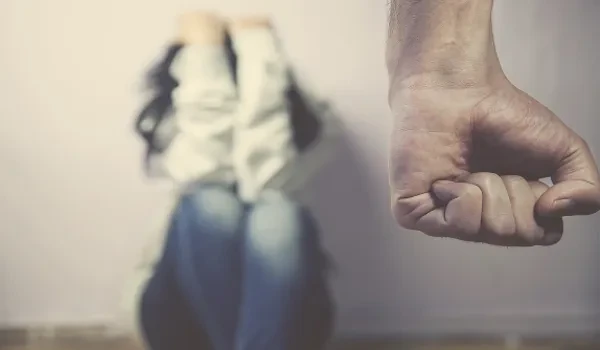 capital-paulista-feminicidios-recorde-2025-outubro Imagem que representa a preocupação com o aumento dos feminicídios na capital paulista, que bate recorde em 2025 até outubro, com destaque para uma mão fechada em sinal de ameaça e uma mulher ao fundo