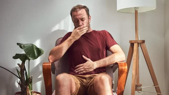 Homem segurando o abdômen e cobrindo a boca, indicando desconforto relacionado a arrotos, causas, sinais de alerta e quando buscar ajuda médica.