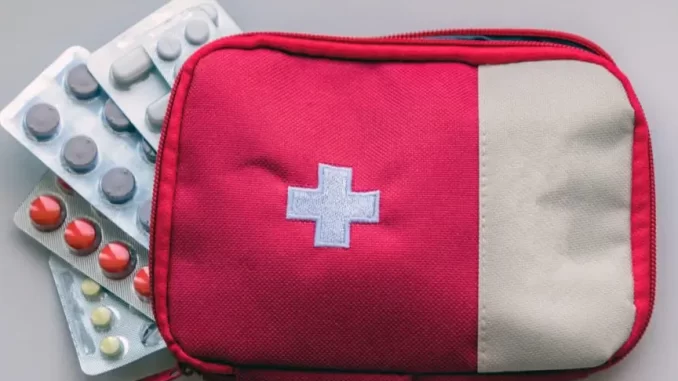 como-transportar-medicamentos-com-seguranca-no-calor-e-no-aviao Mochila vermelha com cruz branca e remédios variados ao lado, ideal para transportar medicamentos com segurança no calor e em viagens de avião.