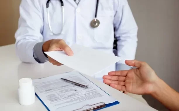Profissional de saúde entregando atestado médico a um paciente, com foco na troca de documentos e orientações sobre atestados de papel.