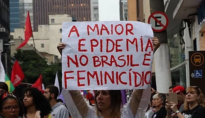 Protestos no Brasil contra feminicídios, com destaque para cartaz que denuncia mais de 700 casos em seis meses, evidenciando a crise de feminicídios no país.