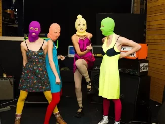 Grupo de oito pessoas usando roupas coloridas e máscaras de ski em ambiente de estúdio de gravação, simbolizando a polêmica envolvendo a classificação da Pussy Riot como organização extremista pela Justiça russa.