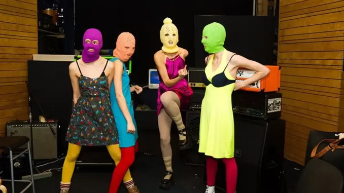 justica-russa-rotula-pussy-riot-organizacao-extremista Grupo de oito pessoas usando roupas coloridas e máscaras de ski em ambiente de estúdio de gravação, simbolizando a polêmica envolvendo a classificação da Pussy Riot como organização extremista pela Justiça russa.