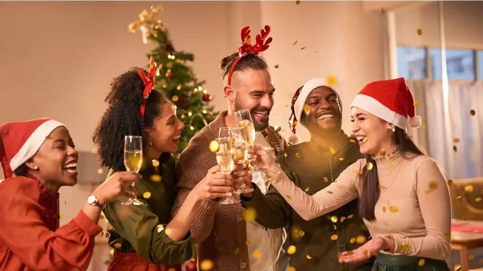 looksfestivosnatalreveillon Grupo de amigos comemorando Natal e Réveillon com looks festivos, usando chapéus de Papai Noel e acessórios natalinos, em ambiente acolhedor.