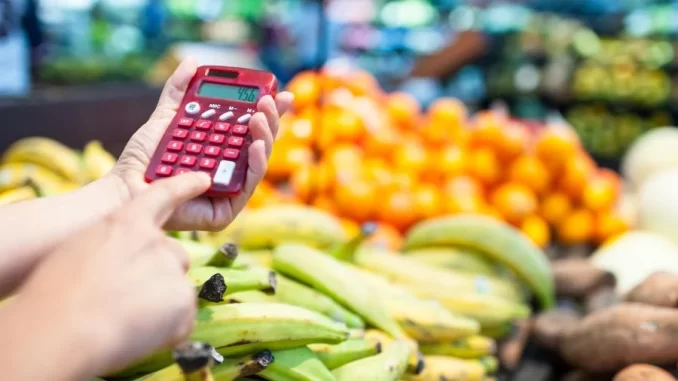 Pessoa usando calculadora no mercado de vegetables, simbolizando a redução na projeção do IPCA para 4,43% em 2025