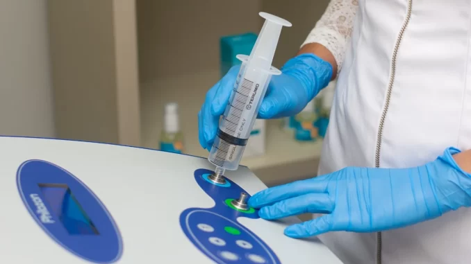 Doutora realizando uma sessão de ozonioterapia com uma seringa em equipamento especializado, evidenciando o uso da técnica sob estudos científicos, dúvidas e riscos.