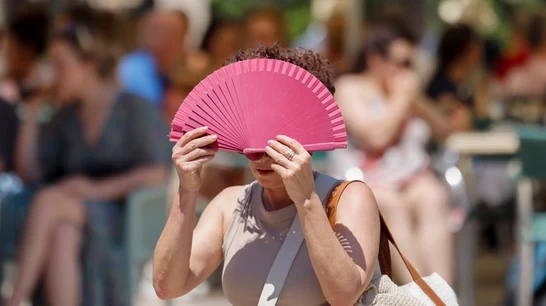 Pessoa usando um leque rosa para se proteger do calor em ambiente ao ar livre, com várias pessoas ao fundo, destacando o impacto do calor extremo no envelhecimento conforme estudo da Universidade do Sul da Califórnia.