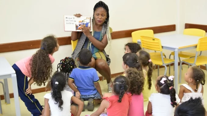 reforma-do-irpf-educacao-basica-abelta-73-por-cento-docentes Professora de educação básica lendo livro para crianças em sala de aula, destacando a inclusão de docentes na reforma do IRPF que isenta 73% desses profissionais.