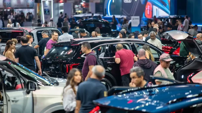 salao-do-automovel-516-mil-visitantes-retorno-2027 Pessoas explorando diversos carros no Salão do Automóvel, que recebeu 516 mil visitantes e retornará em 2027, em uma grande exposição automotiva.