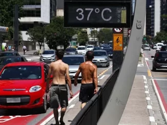 Homens caminhando na calçada de São Paulo sob calor intenso de 37 graus Celsius em dezembro, com termômetro urbano exibindo a temperatura recorde do mês.