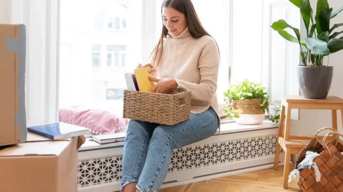 Mulher organizando livros e itens domésticos na janela, promovendo uma casa mais leve e organizada com os sete mandamentos de organização doméstica.