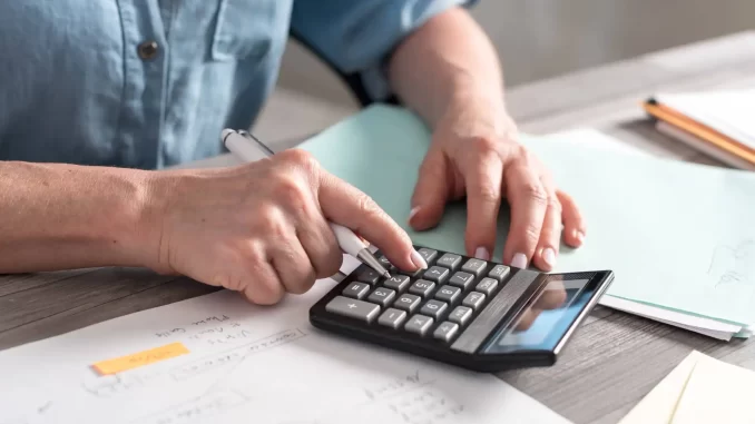 Pessoa usando uma calculadora para planejar o uso do 13º salário na reforma, evitando dívidas, com papéis e caneta ao lado.