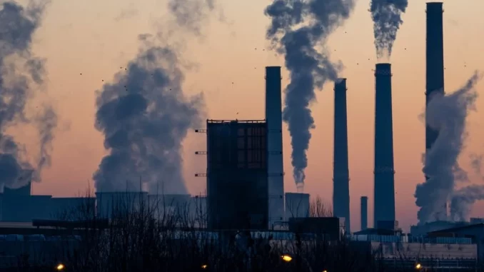 usina-fumarenta-politica-climatica-acordo-paris Vista de uma usine de energia com várias chaminés emitindo fumaça e poluição, simbolizando os desafios ambientais relacionados ao Acordo de Paris e as metas climáticas.