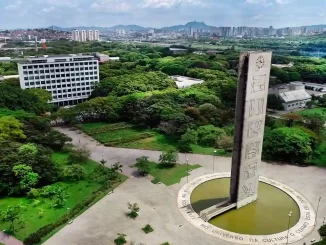 Imagem aérea da Universidade de São Paulo (USP) destacando seu campus com uma escultura emblemática, muitas árvores verdes e uma vista panorâmica da cidade de São Paulo ao fundo, evidenciando sua posição de liderança na América Latina segundo o ranking Times Higher Education.