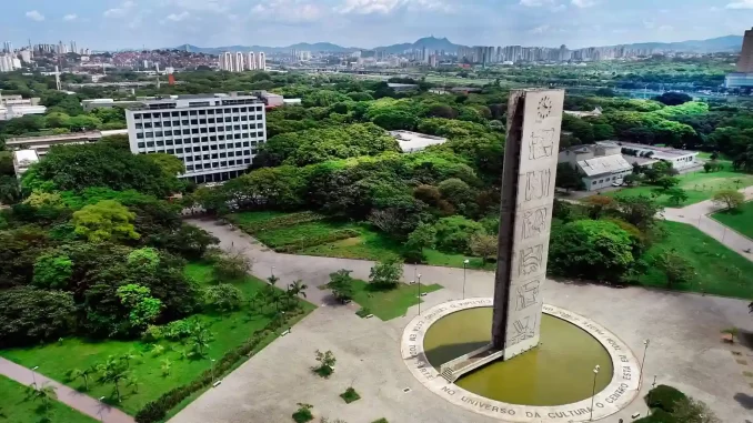 usp-lidera-ranking-times-higher-education-universidades-america-latina Imagem aérea da Universidade de São Paulo (USP) destacando seu campus com uma escultura emblemática, muitas árvores verdes e uma vista panorâmica da cidade de São Paulo ao fundo, evidenciando sua posição de liderança na América Latina segundo o ranking Times Higher Education.