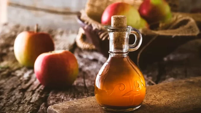 Imagem de uma garrafa de vinagre de maçã em ambiente rústico ao lado de algumas maçãs, indicando pesquisa sobre seu potencial para auxiliar no emagrecimento.