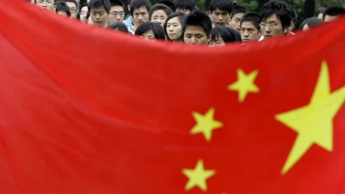Pessoas na China observando bandeira chinesa durante evento relacionado a liderança em IA e revisão de impostos para aumentar natalidade.