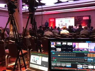 Conferência sobre tendências de live marketing em 2026, com apresentador e público no auditório, equipe de produção e equipamentos de gravação em destaque.