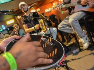 Grupo de músicos de pagode tocando e cantando ao vivo, com destaque para instrumentos como violão e pandeiro, em um ambiente de celebração musical no Brasil.