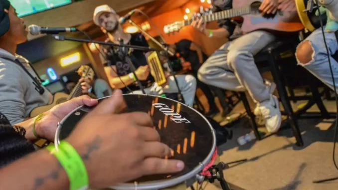 Grupo de músicos de pagode tocando e cantando ao vivo, com destaque para instrumentos como violão e pandeiro, em um ambiente de celebração musical no Brasil.