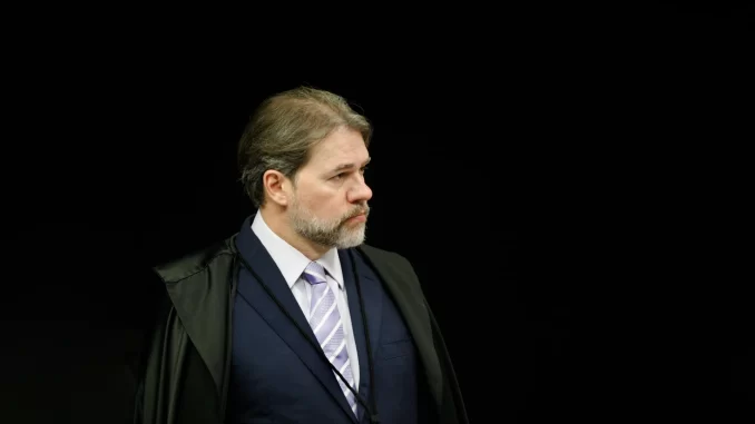 Imagem de um homem com expressão séria, traje formal e cabelo grisalho, aparentando ser uma autoridade judicial, com fundo preto