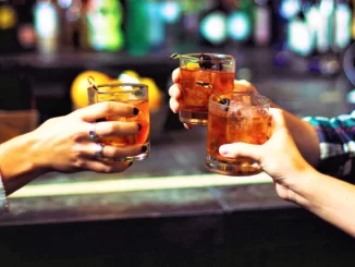 Pessoas brindando com coquetéis em um bar, em referência ao aumento do consumo de álcool na Europa e seu impacto no câncer, segundo a OMS.