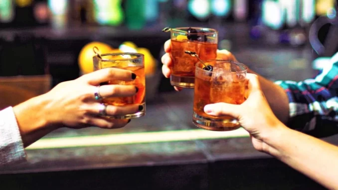 Pessoas brindando com coquetéis em um bar, em referência ao aumento do consumo de álcool na Europa e seu impacto no câncer, segundo a OMS.