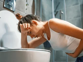 Mulher com dor de estômago segurando a barriga ao lado do banheiro, ilustrando os riscos de intoxicação alimentar e a importância de dicas de higiene para prevenir em casa e fora.