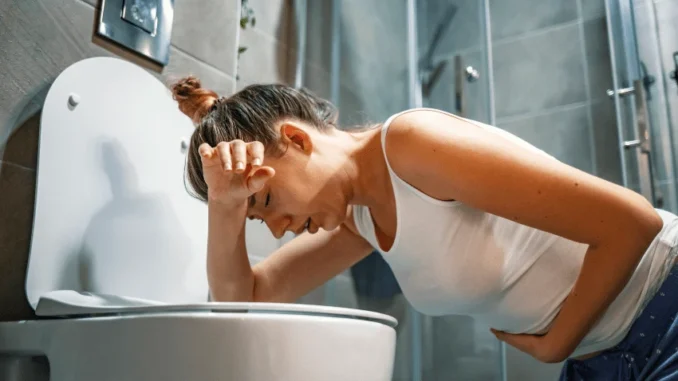 dicas-reduzem-risco-de-intoxicacao-alimentar-em-casa-e-fora-jpg Mulher com dor de estômago segurando a barriga ao lado do banheiro, ilustrando os riscos de intoxicação alimentar e a importância de dicas de higiene para prevenir em casa e fora.