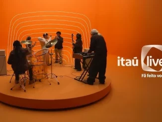 Cena do evento de lançamento do Itaú Live, plataforma de shows do Itaú Unibanco, com músicos tocando em palco com cenário moderno laranja, destacando o protagonismo do banco no mercado de entretenimento ao vivo.