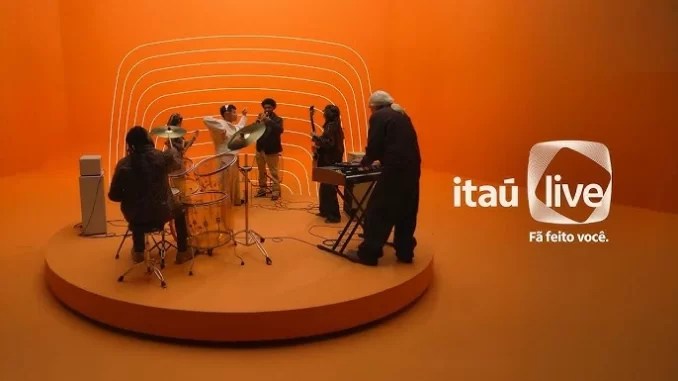 Cena do evento de lançamento do Itaú Live, plataforma de shows do Itaú Unibanco, com músicos tocando em palco com cenário moderno laranja, destacando o protagonismo do banco no mercado de entretenimento ao vivo.