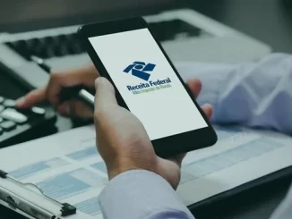 Pessoa verificando o prazo do Imposto de Renda 2026 usando o site da Receita Federal, com documentos organizados ao lado e celular na mão.