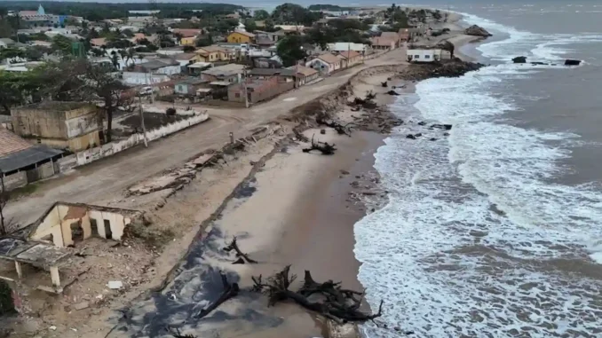 Imagem de uma cidade costeira sendo ameaçada pela elevação do mar, com deslizamentos de terra e árvores destruídas na praia, evidenciando os riscos de desaparecimento até 2030.