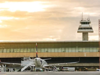 Avião no aeroporto de São Paulo com torre de controle ao fundo, indicando interrupção no controle de tráfego aéreo devido a falha elétrica.