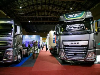Caminhões em destaque em feira de negócios no pavilhão, com estandes ao fundo e iluminação de evento; destaque para o caminhão DAF com faixa visual de marca