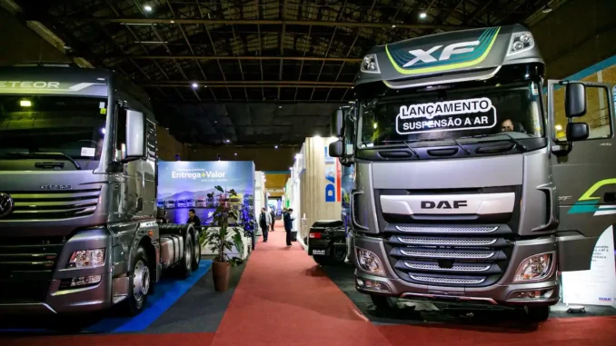 caminhoes-em-feira-de-negocios-pavilhao-destaque-daf Caminhões em destaque em feira de negócios no pavilhão, com estandes ao fundo e iluminação de evento; destaque para o caminhão DAF com faixa visual de marca