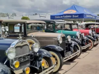 Encontro e Exposição de Veículos Antigos no Campo de Marte, em São Paulo: fila de carros clássicos e caminhões antigos sob tendas e céu nublado, com público ao fundo.